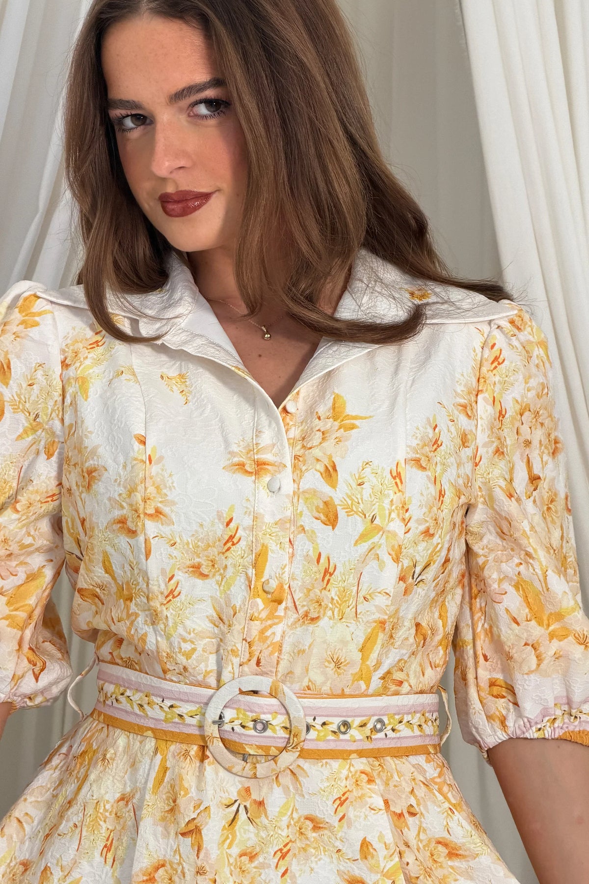 Woman wearing a floral dress with a belt, standing against a neutral background
