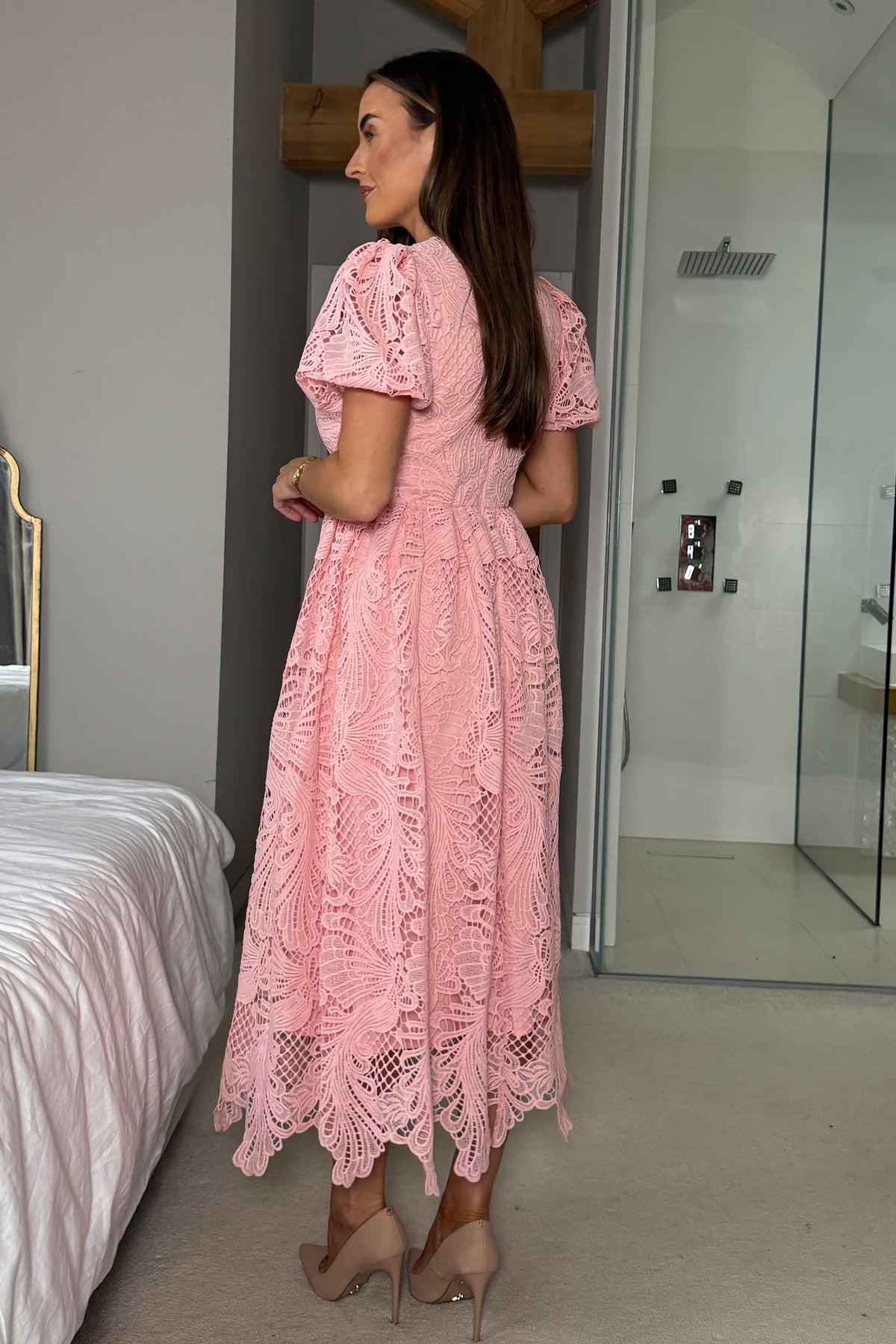 Woman in a pink lace dress standing in a bedroom.