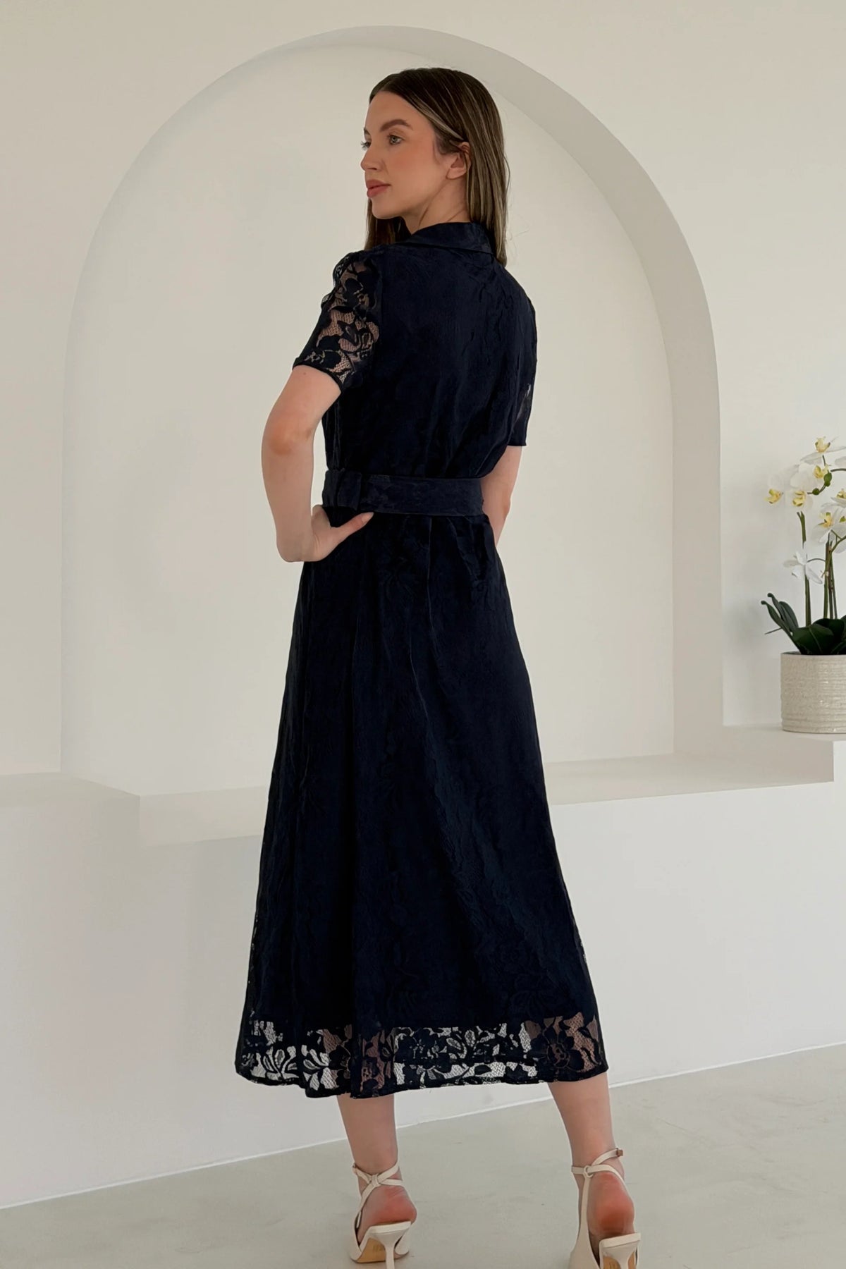 Woman wearing a black dress with lace details in a minimalistic setting