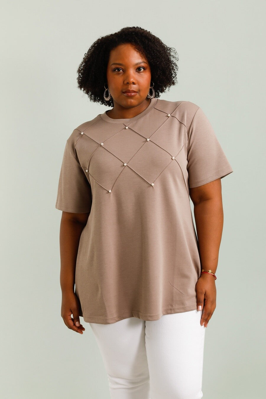 Woman wearing a beige top with pearl embellishments on a plain background