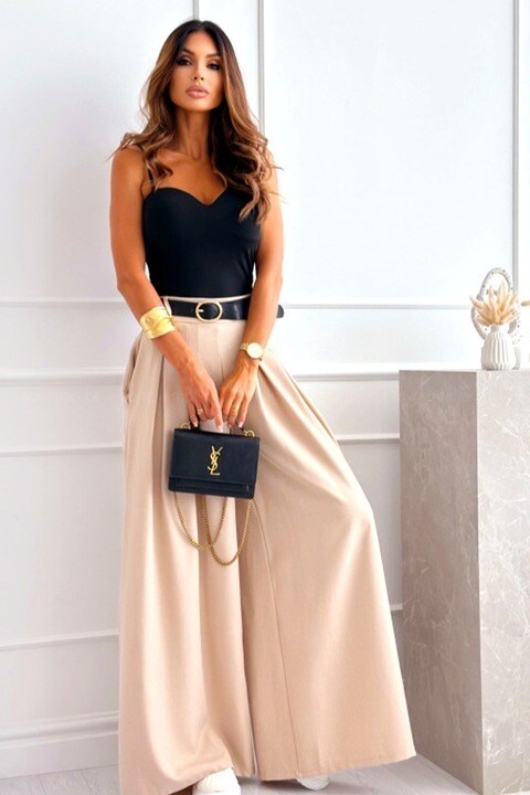 Woman in black top and beige skirt holding a black handbag in a minimalistic setting
