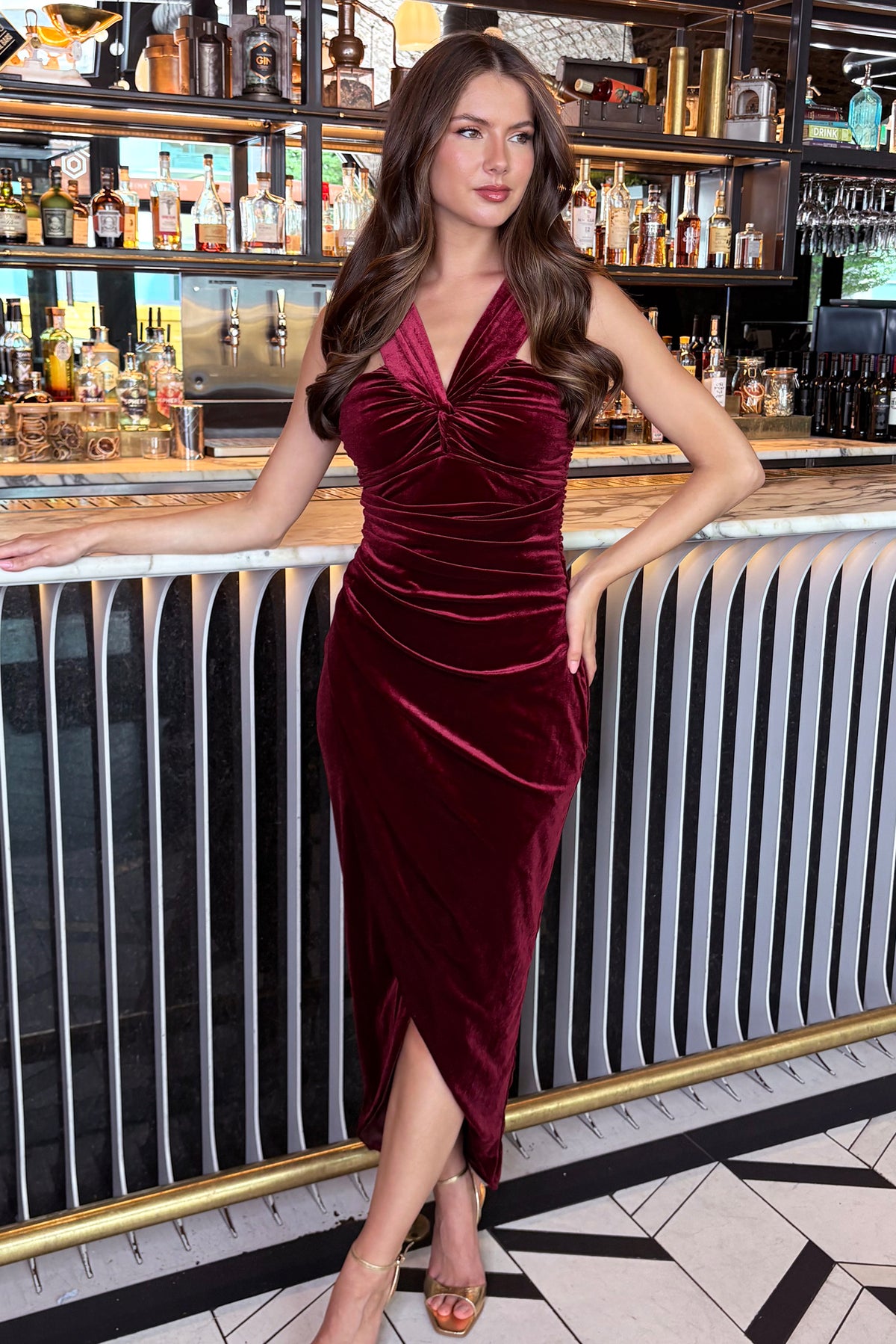 Woman in a burgundy velvet dress standing in a bar setting
