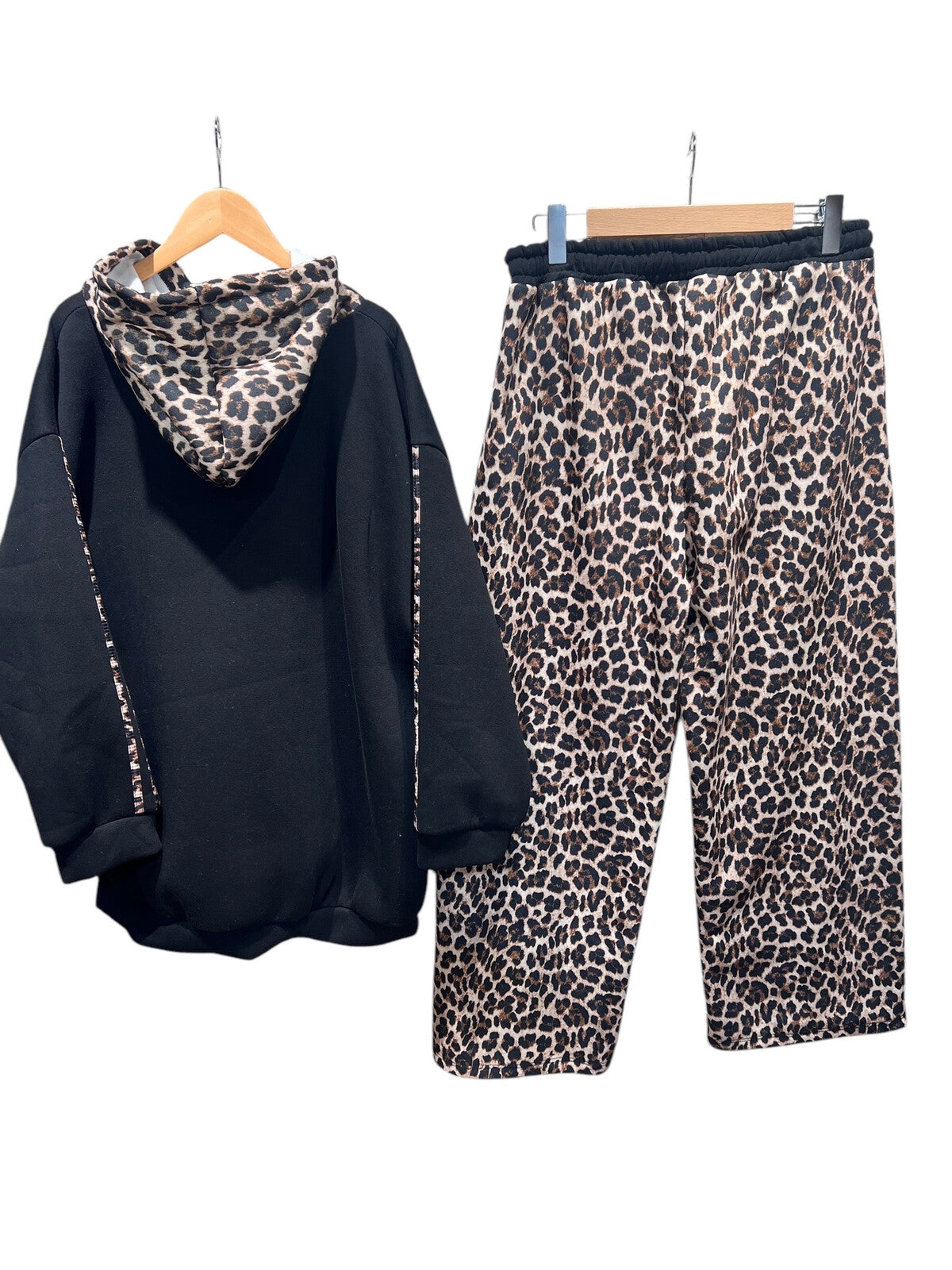 Black hoodie and leopard print pants on hangers against a white background