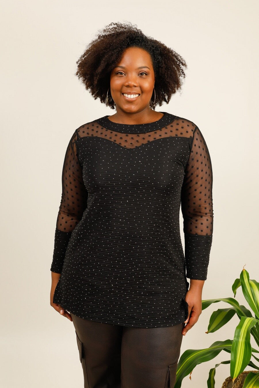 Woman wearing a black polka dot dress with sheer sleeves against a beige background