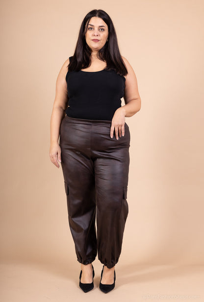 Woman wearing a black top and brown leather pants against a beige background
