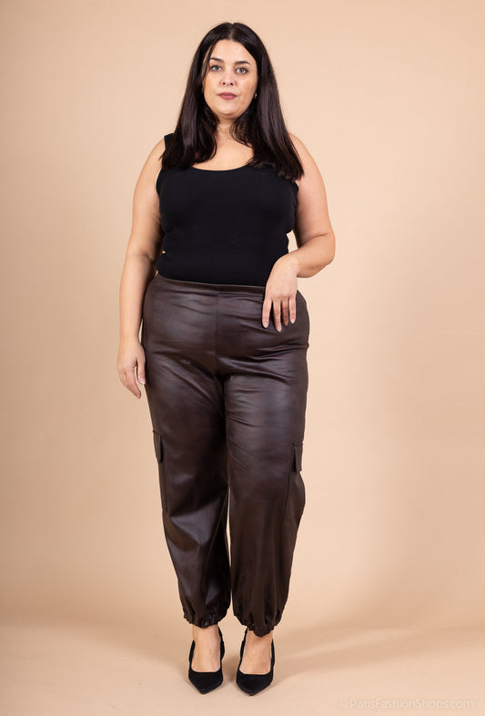 Woman wearing a black top and brown leather pants against a beige background
