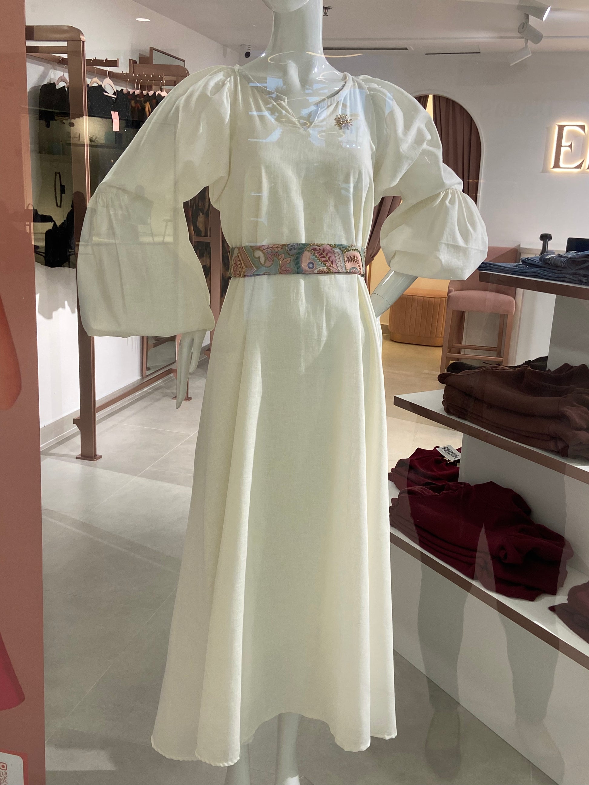 White dress with floral belt on a mannequin in a store setting