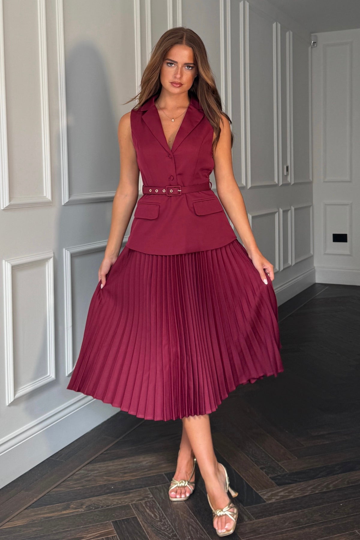 Woman wearing a burgundy pleated dress with a matching vest in an indoor setting.