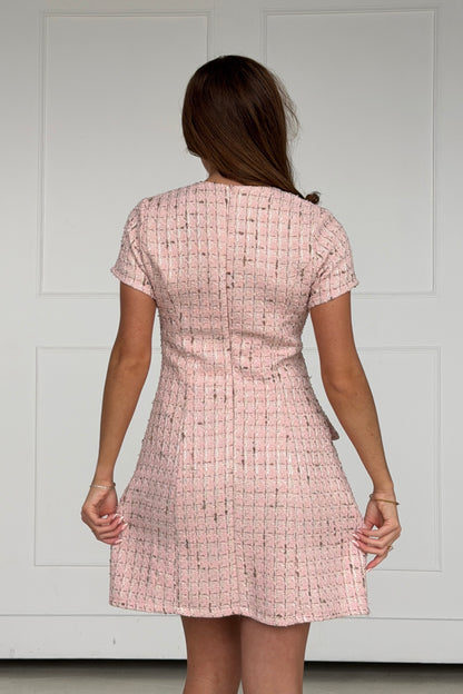 Person wearing a pink checkered dress against a white wall