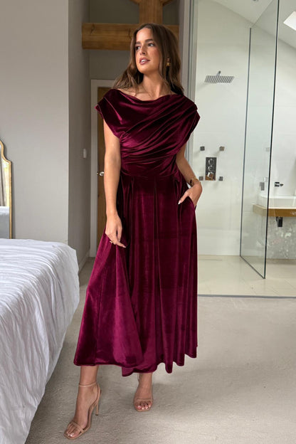 Woman wearing a burgundy velvet dress in a modern interior setting.