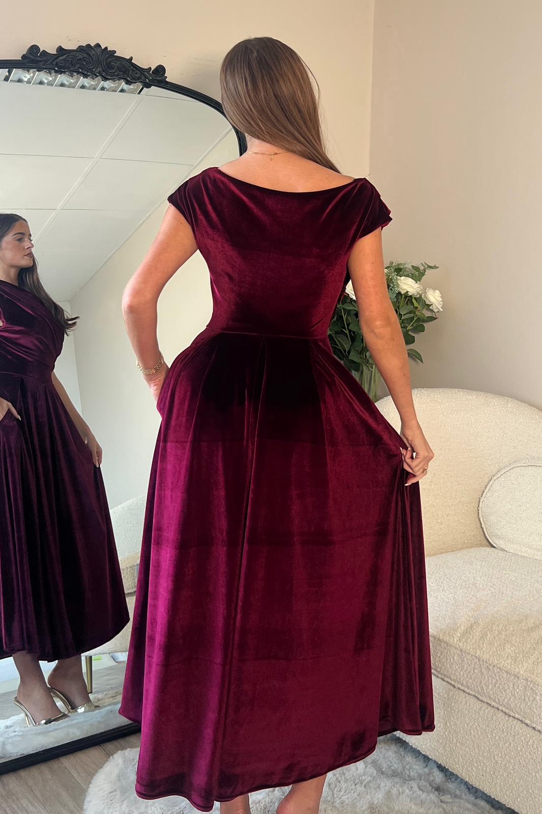 Woman wearing a burgundy velvet dress in a room with a mirror and sofa.