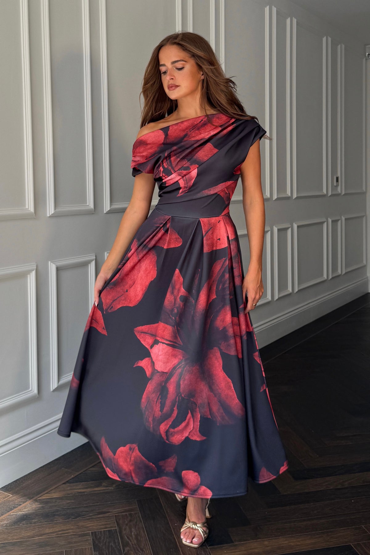 Woman wearing a floral one-shoulder dress in a room with panelled walls.