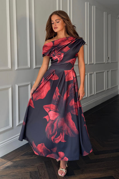 Woman wearing a floral one-shoulder dress in a room with panelled walls.