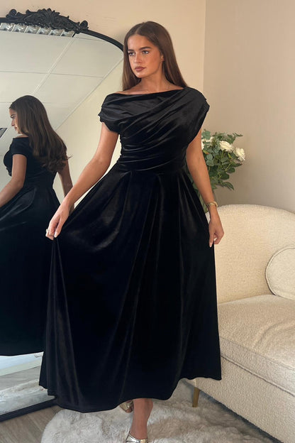 Woman wearing a black dress standing in front of a mirror.