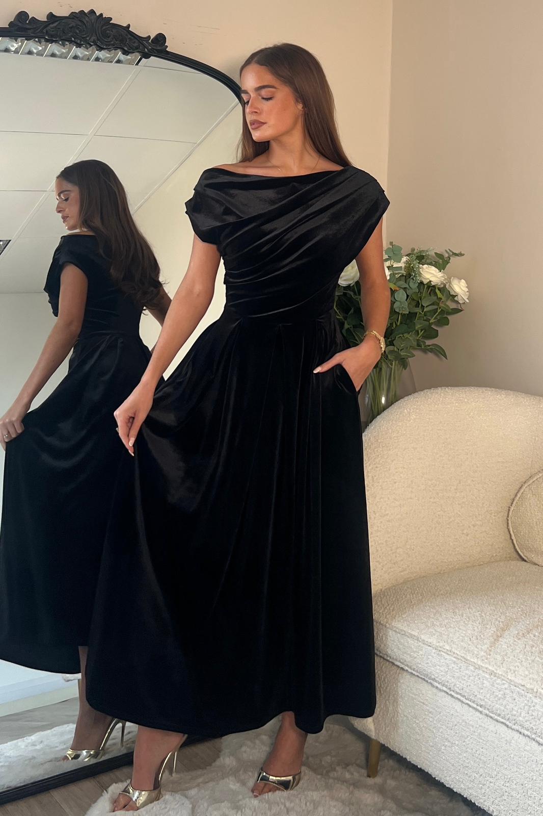 Woman wearing a black evening gown in a room with a mirror and floral arrangement.