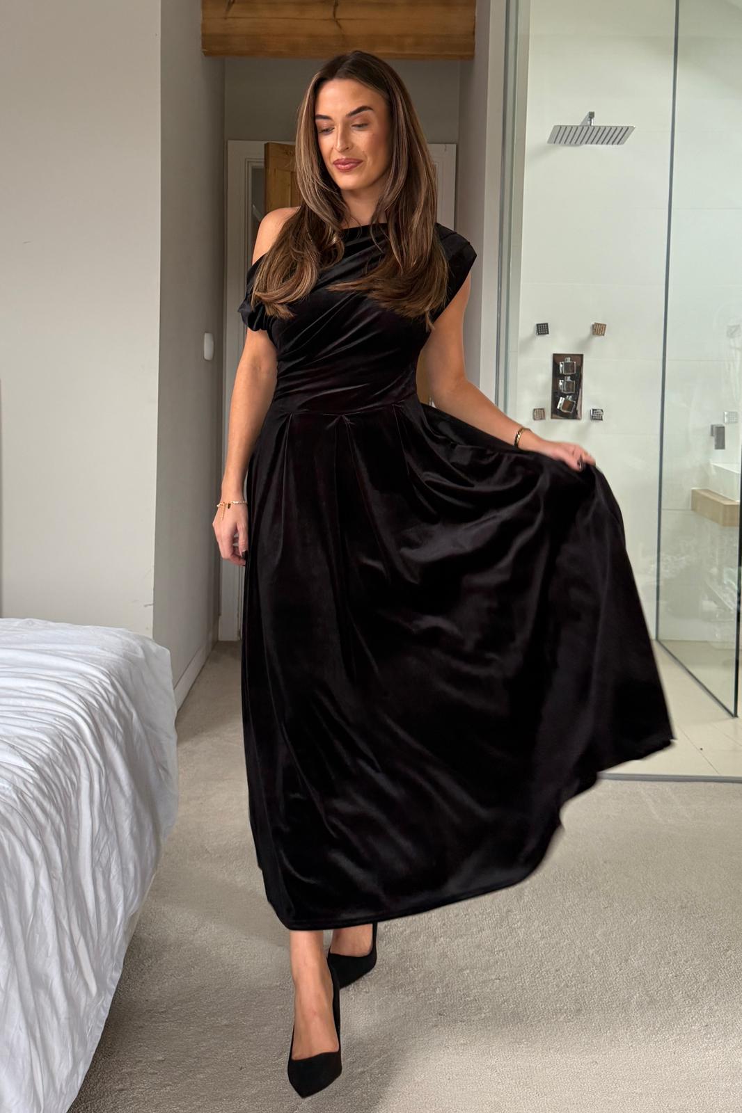 Woman in a black dress standing in a bedroom.