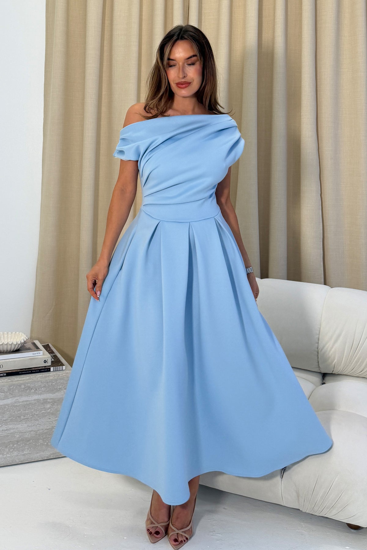 Woman wearing a light blue off-shoulder dress in a living room setting.