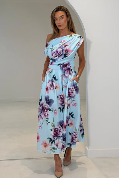 Woman wearing a floral one-shoulder dress in a white room.