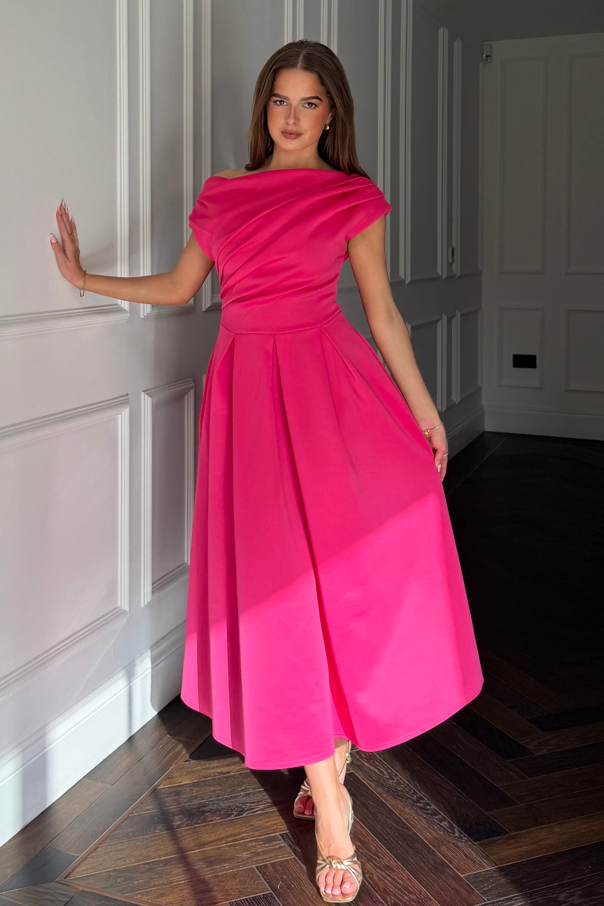 Woman in a bright pink dress standing in a room with white paneled walls.