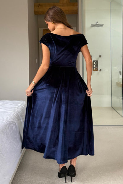 Woman wearing a navy blue dress in a room with a bed and mirror.