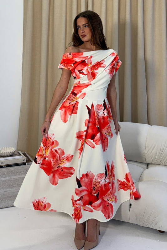 Woman wearing a white dress with red floral patterns in a room.