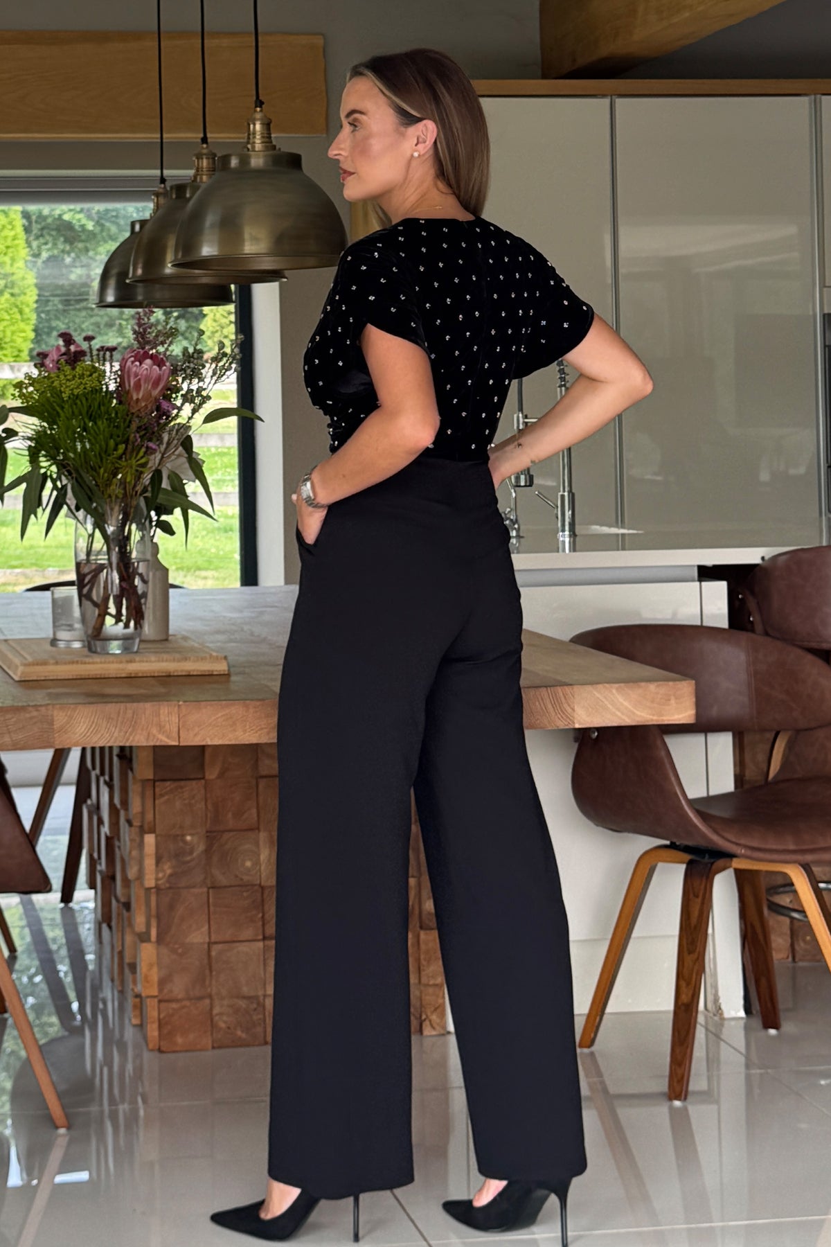 Woman in a black polka dot top and black pants standing in a modern kitchen.