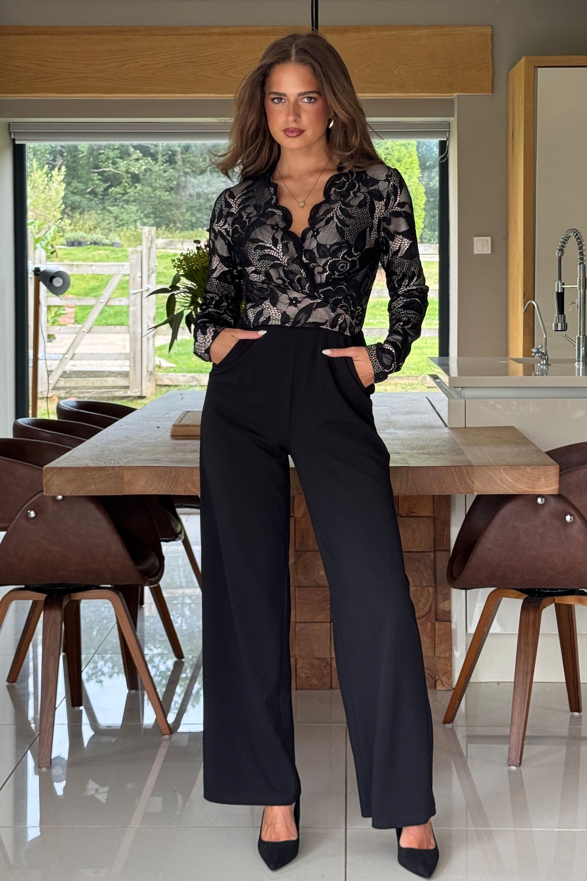 Woman in a stylish outfit sitting at a dining table in a modern kitchen.