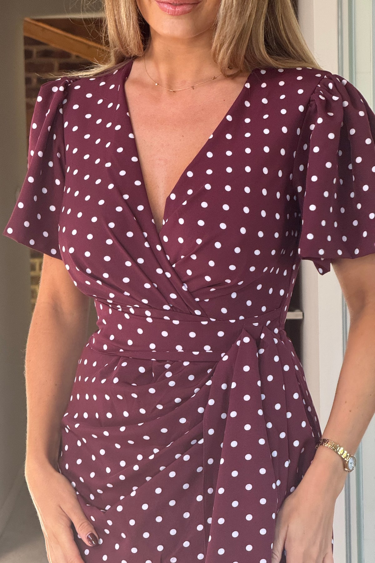 Woman wearing a burgundy dress with white polka dots, standing indoors.