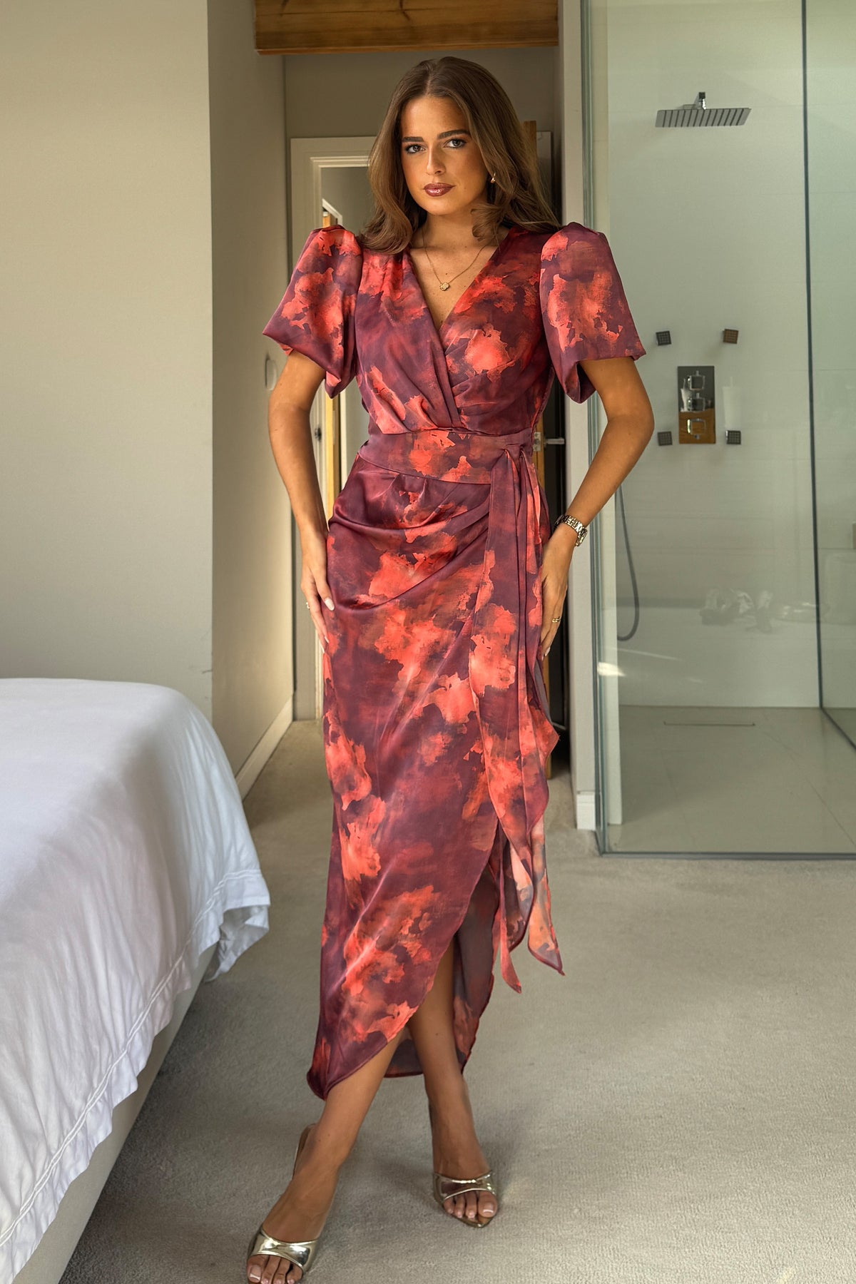 Woman wearing a red and pink patterned dress in a bedroom setting
