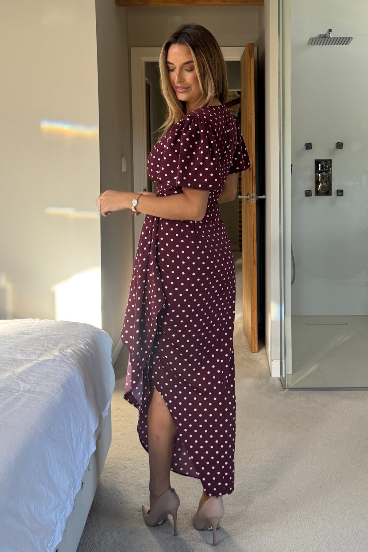 Woman in a burgundy polka dot dress standing in a bedroom.