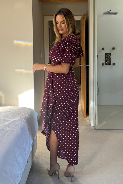 Woman in a burgundy polka dot dress standing in a bedroom.