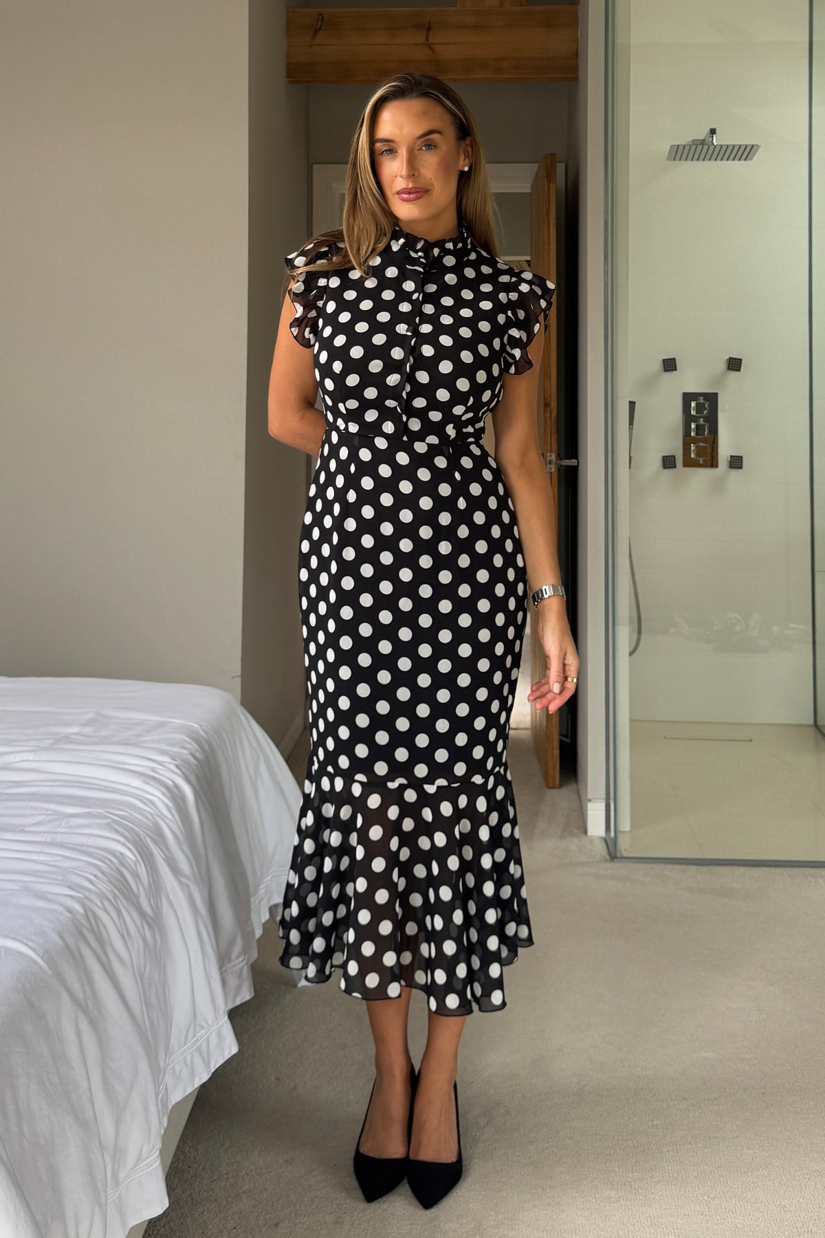 Woman wearing a black and white polka dot dress in a bedroom setting.
