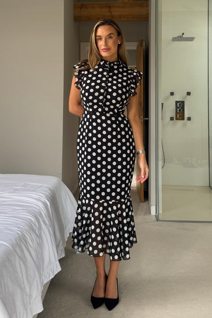 Woman wearing a black and white polka dot dress in a bedroom setting.