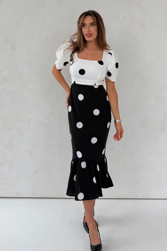 Woman wearing a black and white polka dot outfit against a plain background