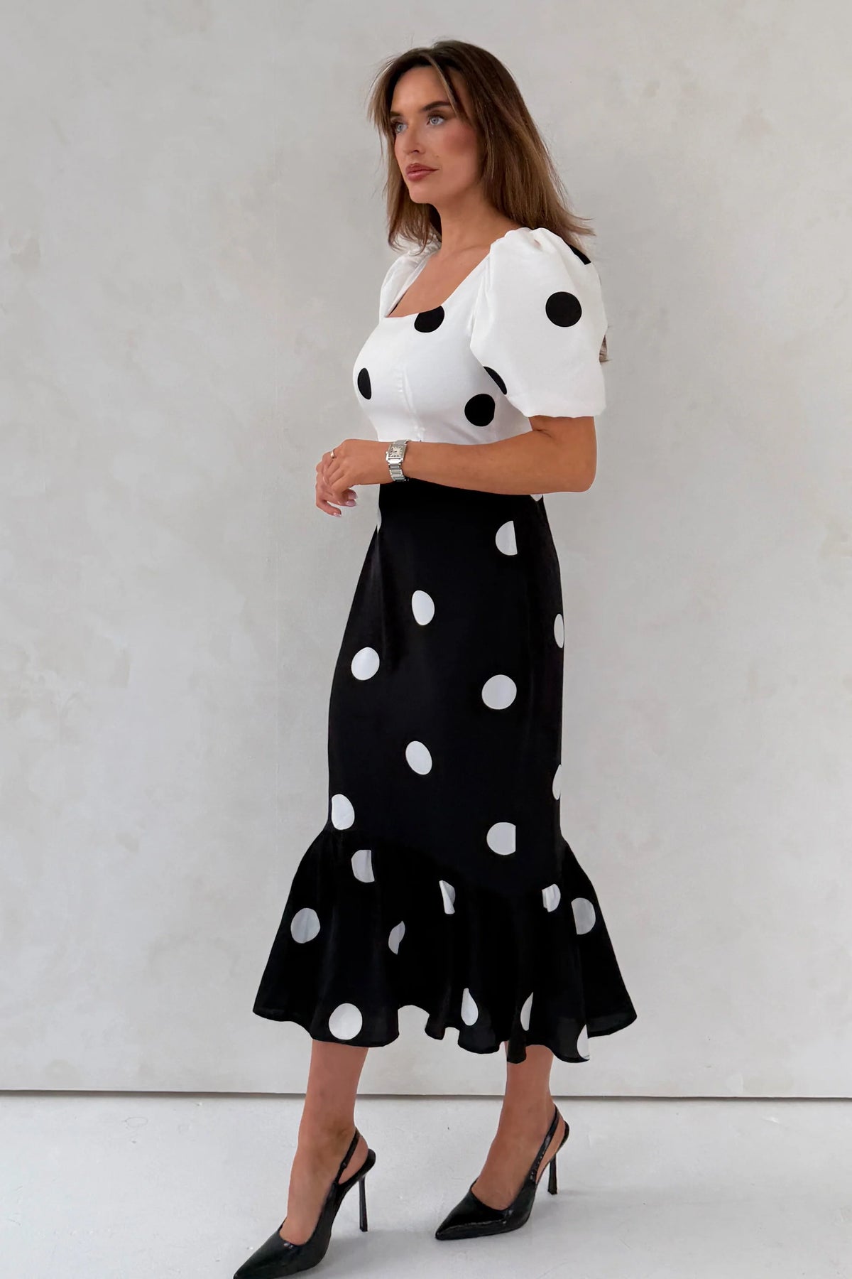 Woman wearing a white top with black polka dots and a black skirt with white polka dots against a light gray background.