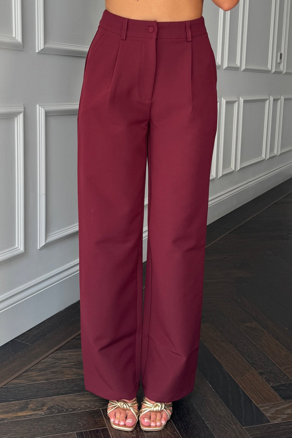 Maroon high-waisted pants worn by a person standing in a room with gray paneled walls.