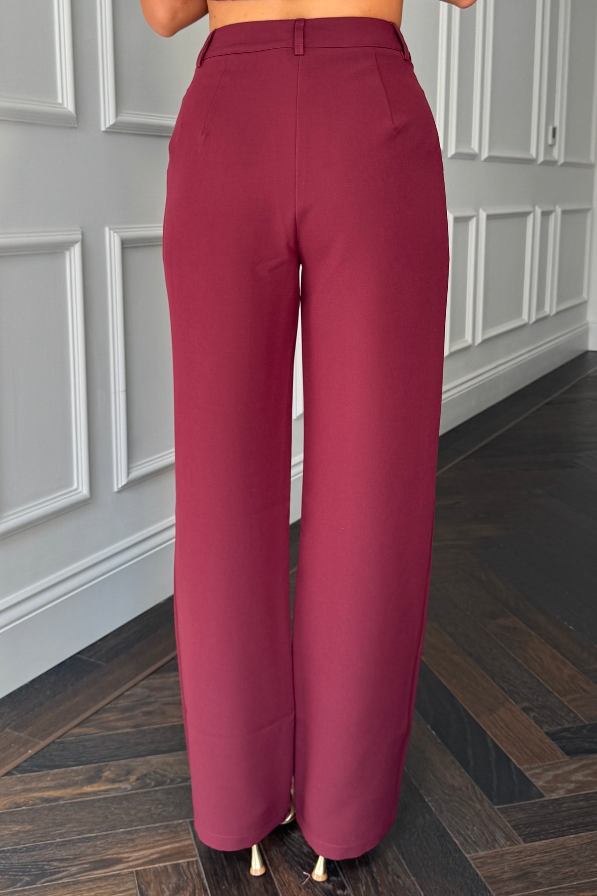 Maroon pants worn by a person standing on a wooden floor with a gray paneled wall in the background.