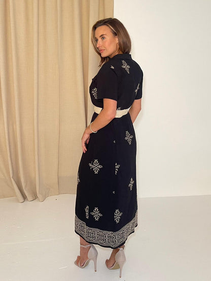 Woman wearing a black dress with white patterns against a neutral background