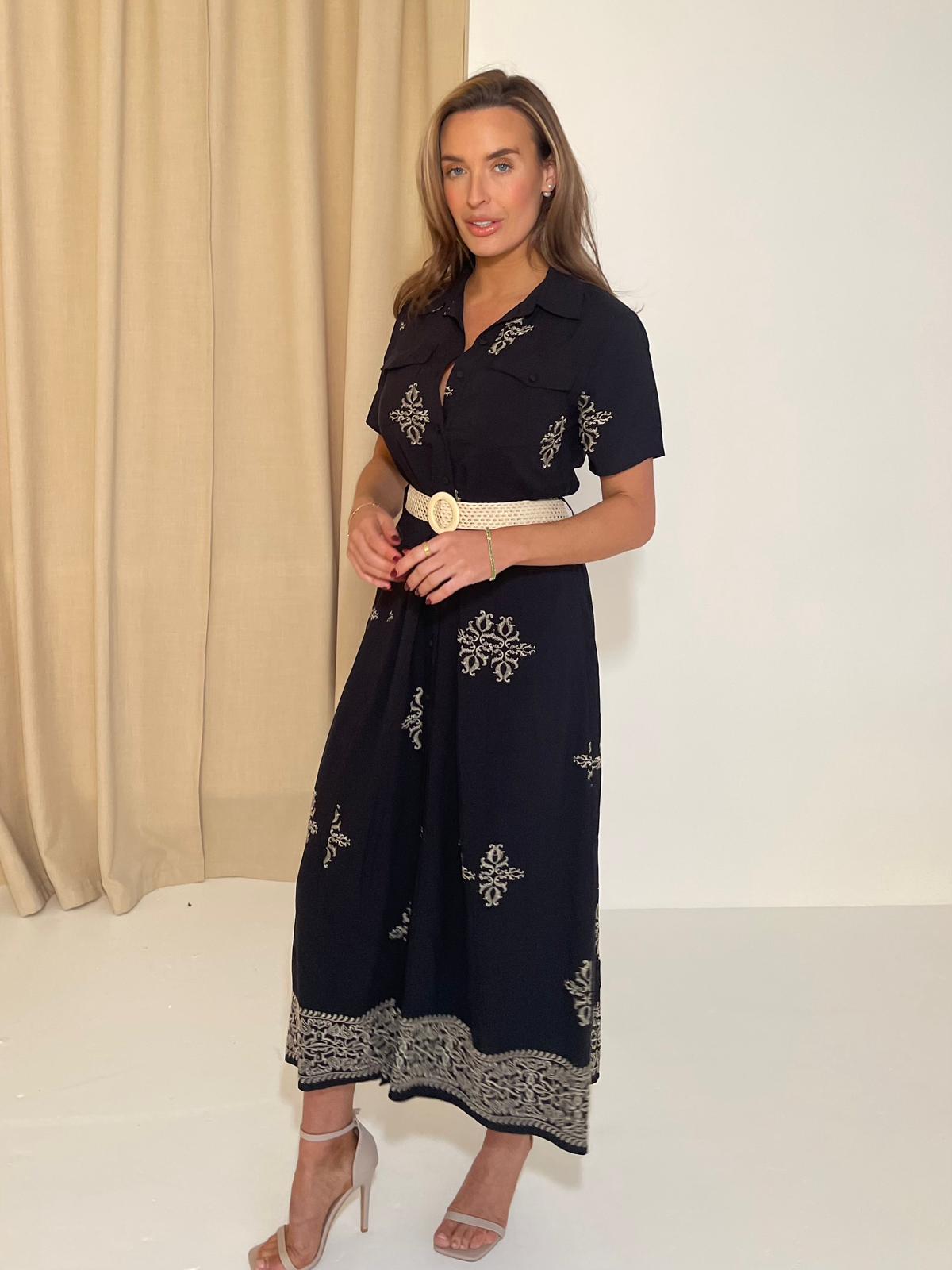 Woman wearing a navy dress with white embroidery against a beige curtain background