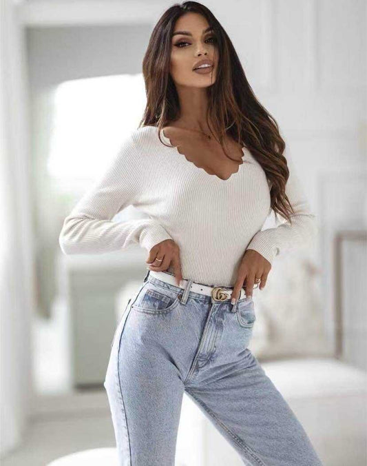 Woman wearing a white sweater and light blue jeans in a bright room.